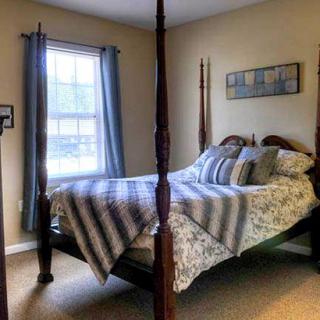 A cozy bedroom featuring a four-poster bed with striped bedding and decorative pillows, a window with blue curtains, and wall art.