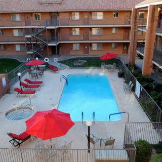 An outdoor hotel swimming pool surrounded by red umbrellas and lounge chairs.