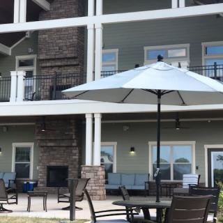 An outdoor patio area featuring tables, chairs, a large umbrella, and a multi-story building in the background.