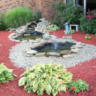 A serene garden featuring a beautiful pond with cascading water, surrounded by vibrant flowers and decorative stones.