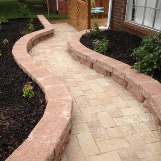A beautifully designed curved paver walkway with a brick retaining wall alongside a garden bed.