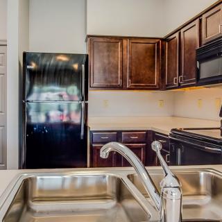 A modern kitchen with a stainless steel sink, wooden cabinets, and black appliances.