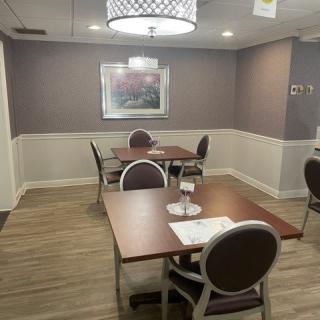 A cozy dining area with neatly arranged tables and chairs, featuring a modern light fixture and wall art.
