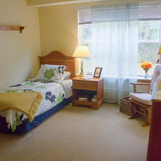 A cozy bedroom with a single bed, nightstand, and window with sheer curtains.