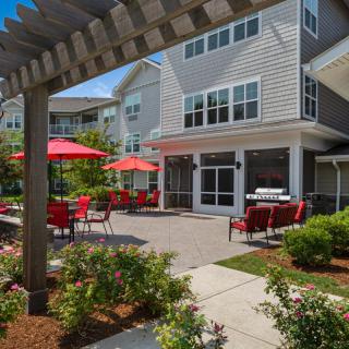 A sunny outdoor patio area with red umbrellas and a residential building backdrop.