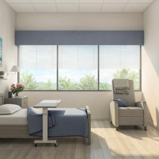 A bright and calming hospital room with a bed, chair, and large windows.