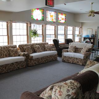 A cozy living room with floral-patterned couches and large windows letting in natural light.