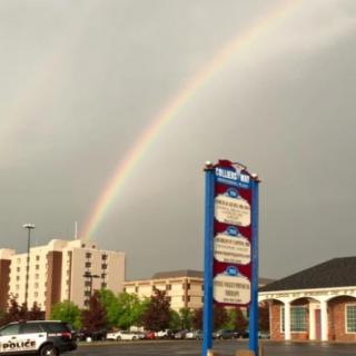 A rainbow arcs over a cityscape featuring tall buildings and a prominent sign.