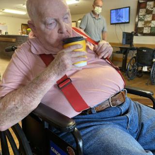 An elderly man enjoying a cup of coffee while seated in a wheelchair.