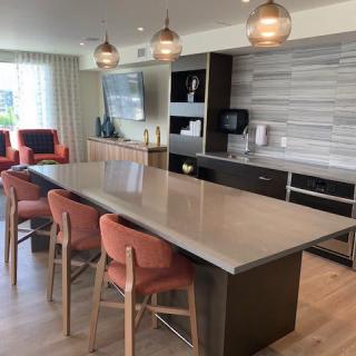 A modern kitchen with a large island and bar stools, featuring pendant lights and an open layout connecting to the living area.