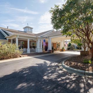 An entrance view of a building with a driveway surrounded by trees and landscaping under a clear sky.