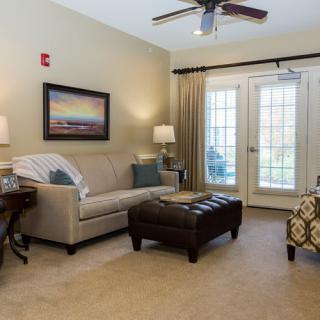 A cozy living room with a sofa, armchair, and a coffee table under a ceiling fan, featuring artwork on the wall and natural light from french doors.