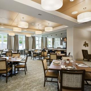 A spacious dining area featuring well-arranged tables and chairs, complemented by modern lighting and large windows.