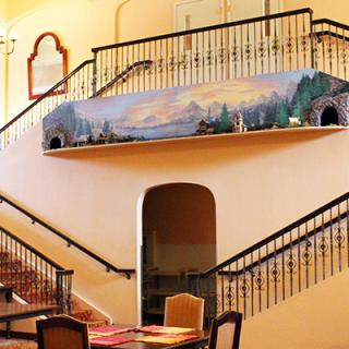 Elegant staircase with model train display and scenic artwork.