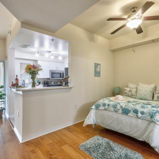 A cozy studio apartment with an open kitchen and a neatly arranged bed.