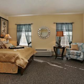A cozy bedroom with a large bed, armchair, and elegant decor including a mirror and lamps.