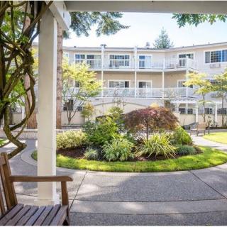 A serene courtyard with lush gardens and outdoor seating in front of an apartment building.