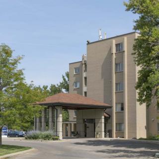 A hotel building surrounded by trees with a covered entrance and a parking area.