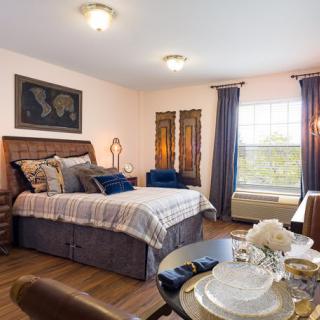 A cozy bedroom with a double bed, decorative pillows, and elegant curtains next to a dining area.