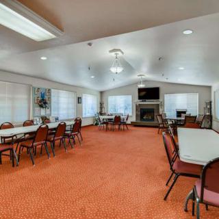 A spacious meeting room with tables and chairs arranged on an orange carpet, featuring large windows and ample lighting.