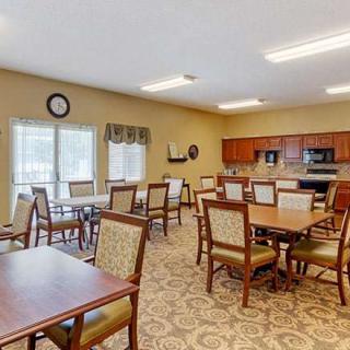 A well-lit dining room with tables and chairs, featuring a kitchen area in the background.
