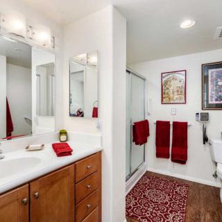 A modern bathroom with red accents, featuring a sink area, mirror, and shower.