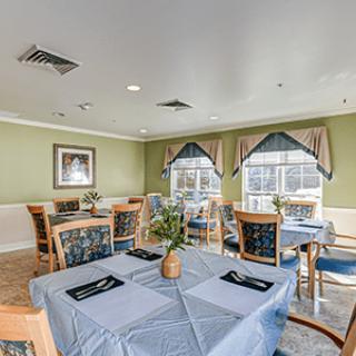 A cozy dining area with tables set for a meal, featuring tablecloths, decorations, and large windows with curtains.