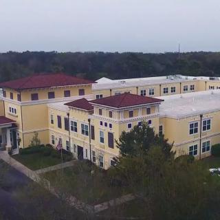 Aerial view of a yellow building with red rooftops surrounded by greenery.