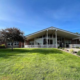 A modern building set against a clear blue sky, surrounded by lush green grass and trees.