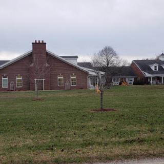 A view of a brick building surrounded by grass and a young tree on a cloudy day.