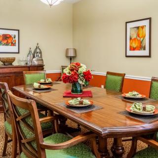 A well-decorated dining room with a wooden table, green cushioned chairs, and colorful artwork on the walls.