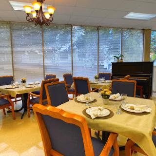 A cozy dining area with set tables, natural light streaming in through the windows, and a piano adding to the ambiance.