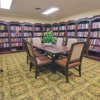 A cozy library room with bookshelves lining the walls and a central table surrounded by chairs.
