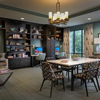 A modern dining room with a table and chairs, surrounded by bookshelves and illuminated by a chandelier.