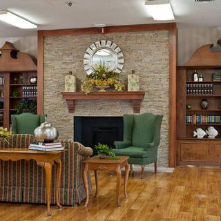 A cozy living room with a stone fireplace, green armchairs, and bookshelves.