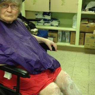 An elderly person sitting in a wheelchair inside a room with medical supplies.