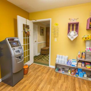 A cozy waiting room with an ATM, yellow walls, and a wooden floor, featuring shelves stocked with magazines and other items.