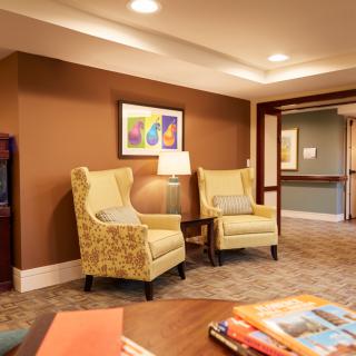 A cozy living room with two armchairs, a lamp, and colorful artwork on the wall.