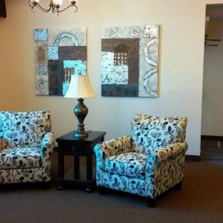 A cozy living room corner with two patterned armchairs, a lamp on a side table, and abstract artwork on the wall.