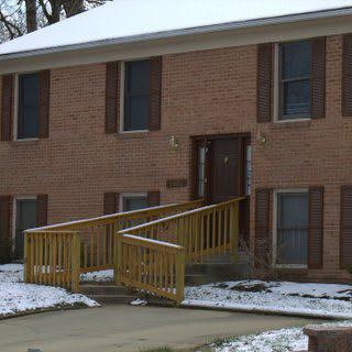 A brick house with a wooden accessibility ramp surrounded by light snow.