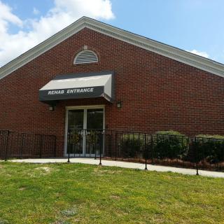 A brick building with an awning over the entrance, surrounded by grass and shrubs.