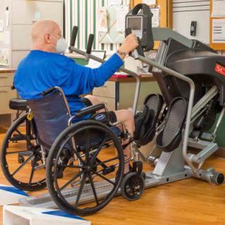 An elderly person in a wheelchair using exercise equipment for rehabilitation.