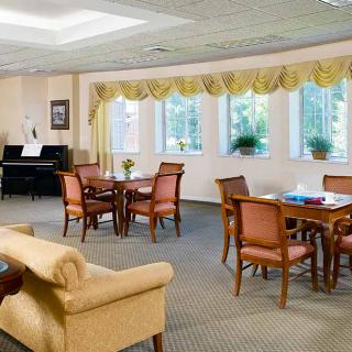 A cozy and spacious living area with multiple tables, chairs, a sofa, and a piano by large windows adorned with curtains.