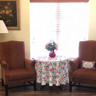 A cozy living room setup with two armchairs, a floral-covered table, and a vase of flowers by the window.
