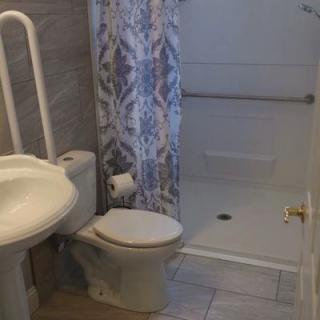 A bathroom featuring a sink, toilet, shower with a curtain and handrail.