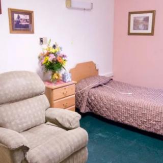 A cozy bedroom with a single bed, recliner chair, and a nightstand adorned with flowers.