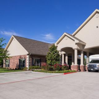A spacious residential building with a driveway and a parked vehicle under a clear blue sky.