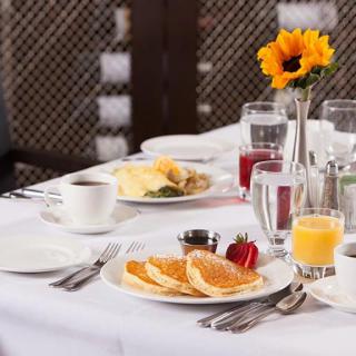 A breakfast table set with pancakes, orange juice, coffee, and a sunflower centerpiece.