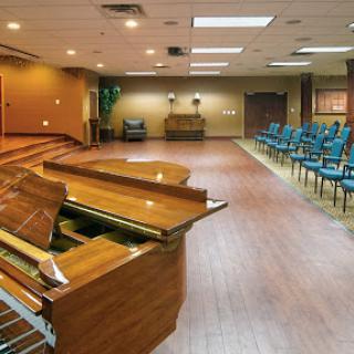 An interior view of a performance space featuring a piano and rows of blue chairs.