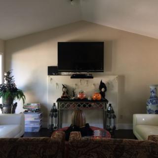 A cozy living room featuring a television above a decorated fireplace with lanterns, candles, and pumpkins.